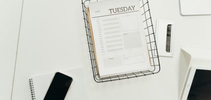 Top view of a neat office desk with a Tuesday planner, smartphone, and gadgets, perfect for scheduling and organization.