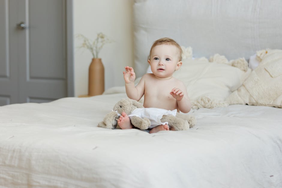 Cute baby sitting on a bed with plush toy, indoors.