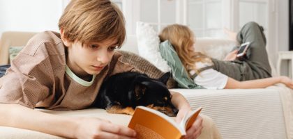 A boy with a dog reading a book on a couch, creating a cozy indoor scene.