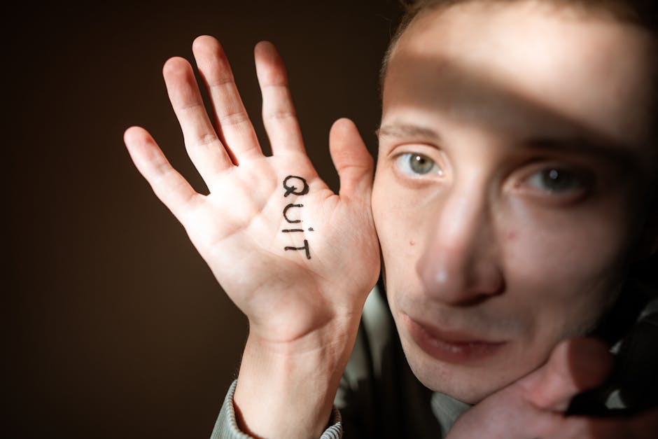 Close-up of a man showing the word 'Quit' on his palm, with dramatic lighting
