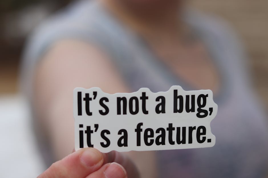 Close-up of a hand holding a sticker with a humorous tech message: 'It's not a bug, it's a feature.'