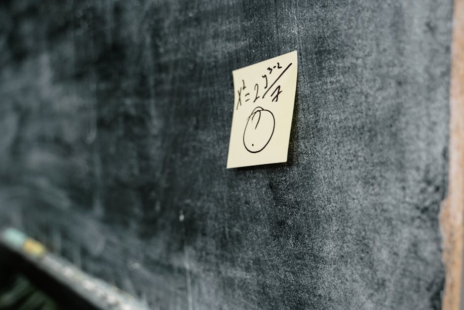 Close-up of a blackboard with a sticky note displaying a handwritten equation and drawing.