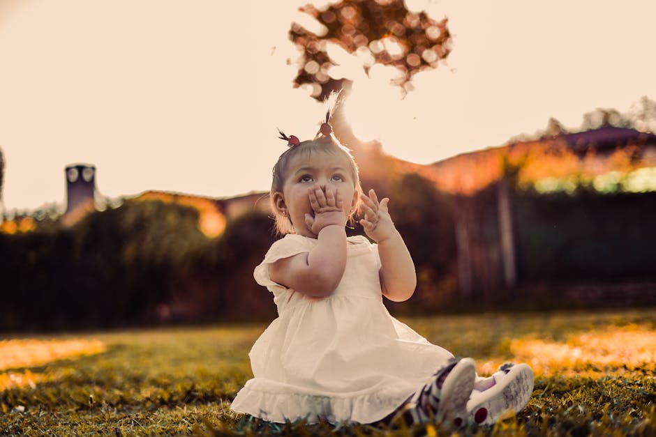 A cute baby girl sitting on grass in the golden light of sunset, expressing wonder and joy.
